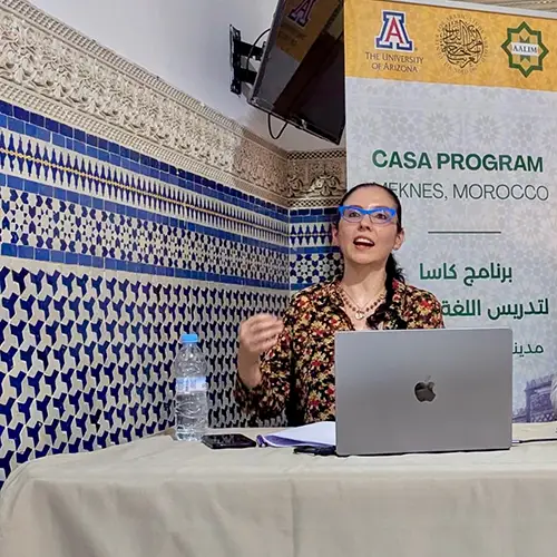 A woman speaker talking from behind a table with a laptop
